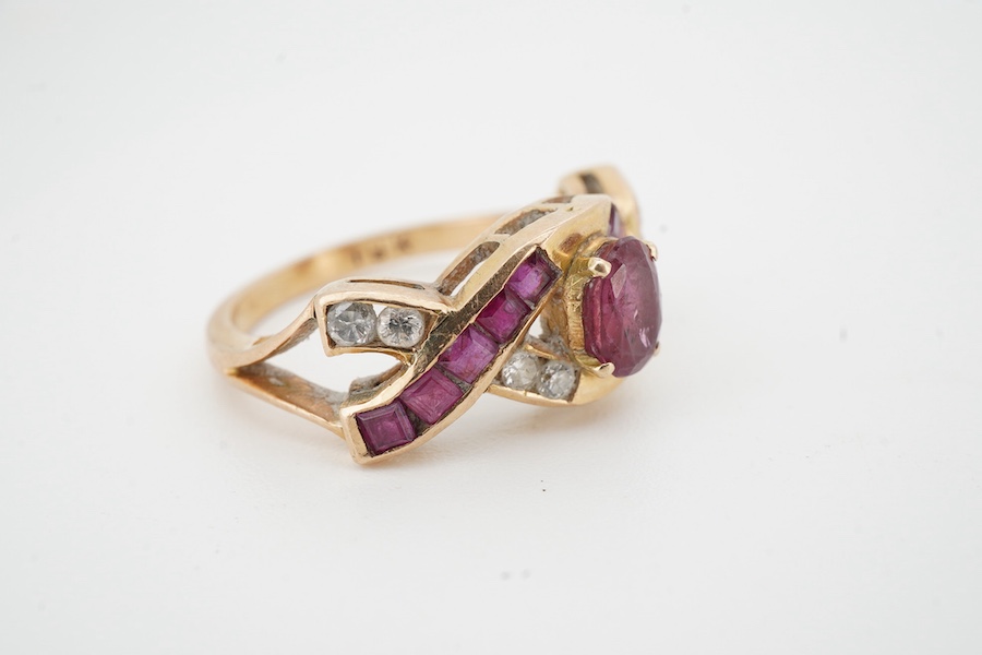 A ruby and diamond ring, of woven design, centring on an oval ruby, to a band set with calibré-cut rubies and brilliant-cut diamonds, mounted in gold, size N1/2, stamped 18K, gross weight 4 grams